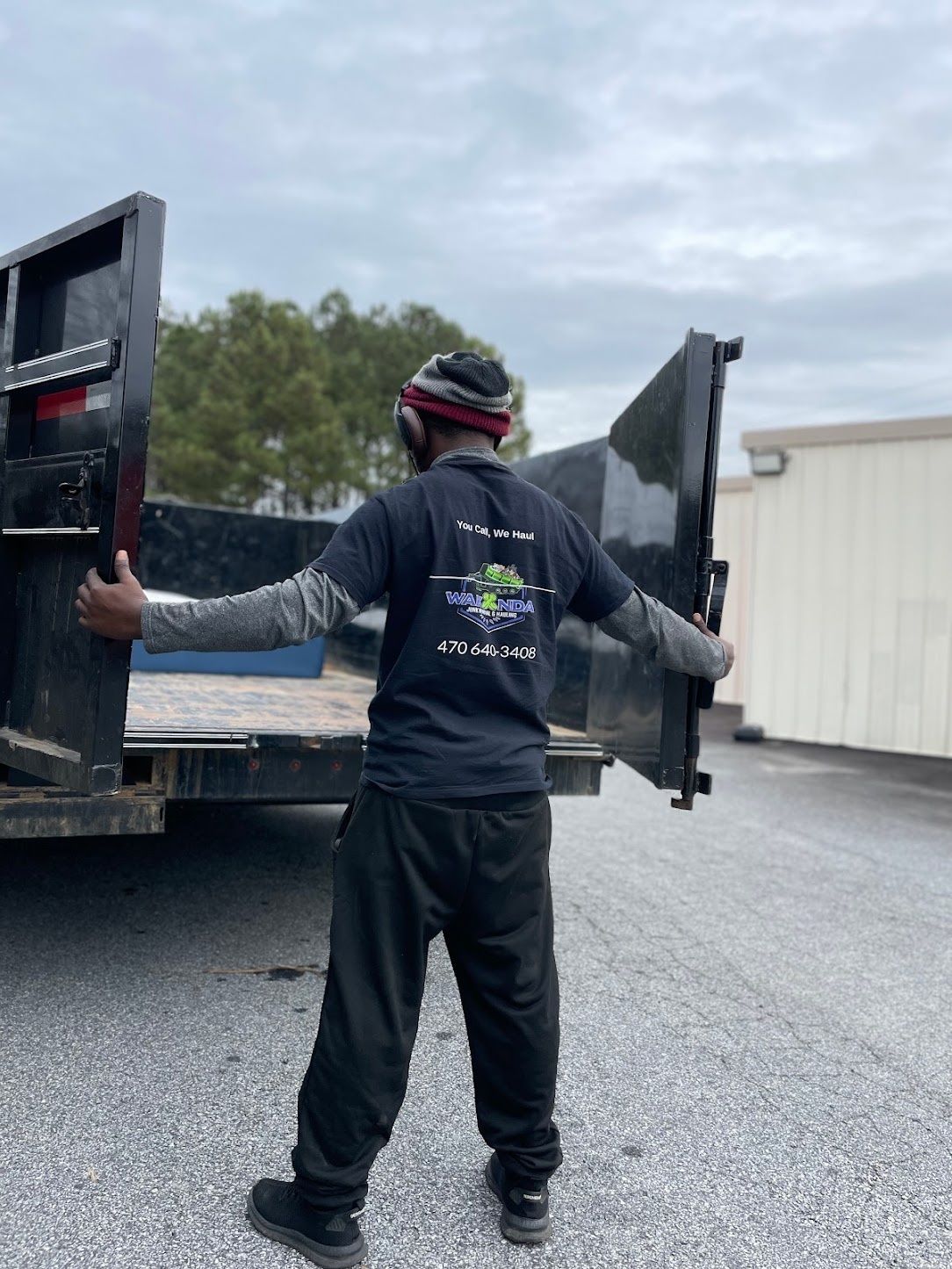 A Wakanda Junk Removal crew member in a Wakanda shirt opening the dump trailer